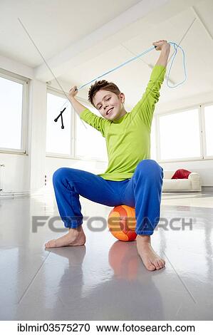 Stock Image - "Boy in casual clothes sitting on ball, holding a rope, Germany, Europe". Fotosearch