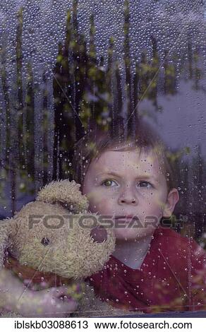 "Boy looking out of a window with water drops, holding a stuffed animal in his arms" View Large Photo Image Stock Image - "Boy looking out of a window with water drops, holding a stuffed animal in his arms". Fotosearch