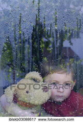 "Boy looking sadly out of a window with water drops, holding a stuffed animal in his arms" View Large Photo Image Stock Photo - "Boy looking sadly out of a window with water drops, holding a stuffed animal in his arms". Fotosearch