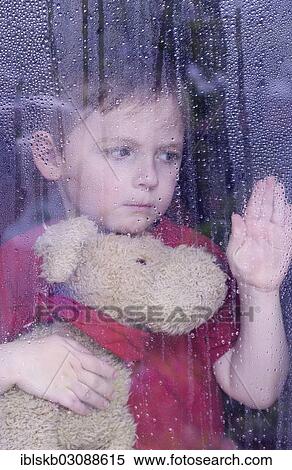 "Boy looking sadly out of a window with water drops, holding a stuffed animal in his arms" View Large Photo Image Stock Photography - "Boy looking sadly out of a window with water drops, holding a stuffed animal in his arms". Fotosearch