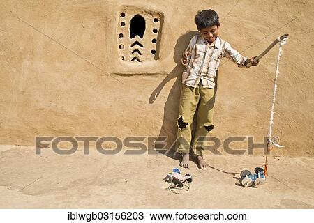 Stock Image - "Boy playing with a home-made toy car outside a mud house, Wuste Thar, Rajasthan, India, Asia". Fotosearch