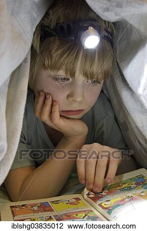 Boy reading a comic with a head lamp under the duvet View Large Photo Image Stock Image - Boy reading a comic with a head lamp under the duvet. Fotosearch