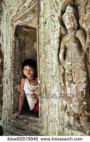 Stock Photograph - "Boy sitting next to stone carvings in a historic temple, Angkor Wat temple complex, Siem Reap, Cambodia, Asia". Fotosearch