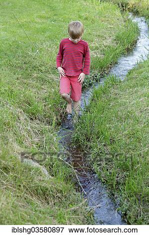 Stock Photo - "Boy wades through a creek, Germany, Europe". Fotosearch