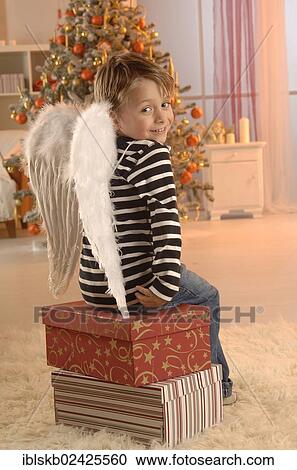Boy wearing angel wings sitting on gifts in front of a Christmas tree View Large Photo Image Stock Image - Boy wearing angel wings sitting on gifts in front of a Christmas tree. Fotosearch
