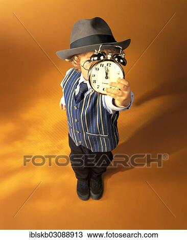 Stock Image - "Boy wearing business clothes holding an alarm clock showing eleven fifty-five, just before high noon". Fotosearch