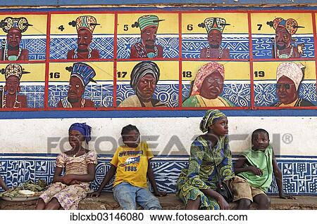 Stock Image - "Boys and girls sitting in front of the row of ancestors on the Sultan's Palace of Foumban, Foumban, West Region, Cameroon, Africa". Fotosearch