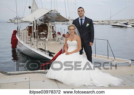 Stock Image - Bride and groom posing in front of a yacht in a marina. Fotosearch