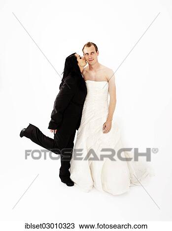 Stock Image - "Bride wearing a suit kissing a groom wearing a wedding dress on the cheek, exchange of wedding clothing, Austria, Europe". Fotosearch