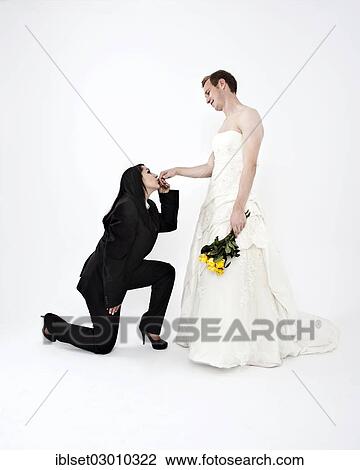 Stock Image - "Bride wearing a suit kissing the hand of a groom wearing a wedding dress, exchange of wedding clothing, Austria, Europe". Fotosearch