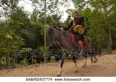 Picture - "Buddhist monk on horseback with a begging bowl collecting alms in the morning, temple and monastery of Wat Phra Archa Thong or Golden Horse Temple, Mae Chan, Chiang Rai Province, Northern Thailand, Thailand, Asia". Fotosearch