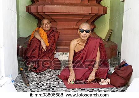 Stock Photo - "Buddhist monks sitting in front of a place of worship in a temple, one of them wearing Ray Ban sunglasses, Yangon, Myanmar, Asia". Fotosearch