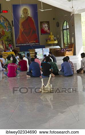 Stock Image - "Buddhists praying in a temple, dog lying on its back and stretching its paws in the air behind them, Rajban Bihar Pagoda, Kaptai Lake, Rangamati, Chittagong Hill Tracts, Bangladesh, South Asia, Asia". Fotosearch