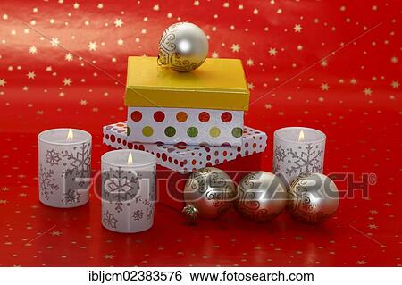 Stock Photograph - "Burning candles standing on red Christmas wrapping paper, with presents and baubles". Fotosearch
