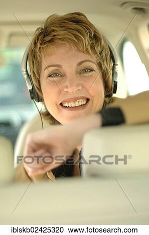 Stock Image - Business woman with headphones sitting in a car. Fotosearch