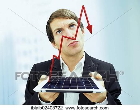 Stock Image - "Businessman with a serious face holding an iPad with a plunging stock chart, symbolic image for economy, recession, crisis". Fotosearch