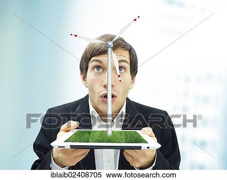 Stock Photography - "Businessman with a surprised face holding an iPad with a wind turbine, symbolic image for sustainable energy". Fotosearch