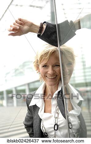 Stock Photo - "Businesswoman, 40-50, leaning against a glass wall". Fotosearch