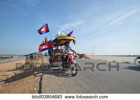 Stock Image - "Cambodian monks and novices on a tuktuk with Buddhist flags and national flags of Cambodia at a protest, Kampong Cham Province, Cambodia, Asia". Fotosearch