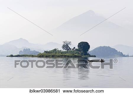 "Canoe glides in the morning mist on Mutanda Lake in front of Muhavura volcano at the border with Rwanda, Kisoro, southwestern Uganda" View Large Photo Image Stock Image - "Canoe glides in the morning mist on Mutanda Lake in front of Muhavura volcano at the border with Rwanda, Kisoro, southwestern Uganda". Fotosearch