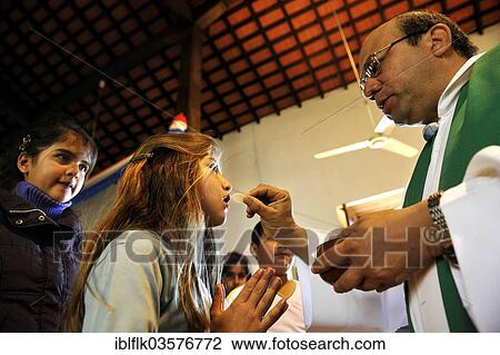 Stock Image - "Catholic children's mass, priest giving communion to a girl, San Joaquin, Caaguazu Department, Paraguay, South America". Fotosearch