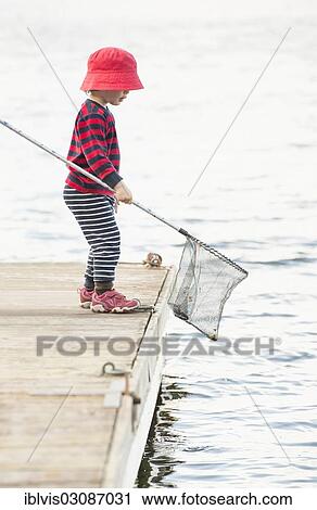 Stock Image - "Child standing on dock by the sea with fishing net in hand, Stockholm, Sweden, Europe". Fotosearch