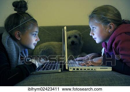 Stock Image - Children at the computer, lying on the sofa in the dark. Fotosearch