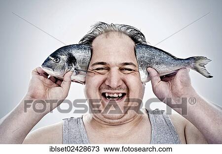 Stock Image - "Chubby man holding a fish next to his head, laughing". Fotosearch