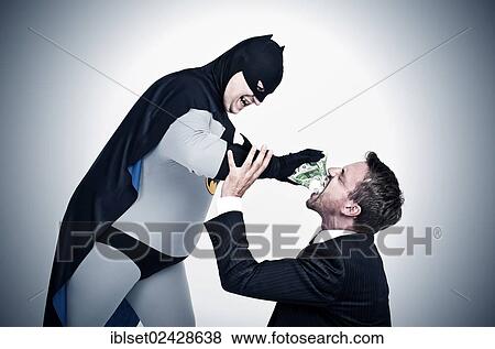 Chubby superhero wearing a Batman costume stuffing money into the mouth of a man wearing a suit View Large Photo Image Stock Photo - Chubby superhero wearing a Batman costume stuffing money into the mouth of a man wearing a suit. Fotosearch