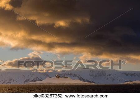 Stock Image - "Clouds and glaciated mountains in the Gerlache Strait in the evening light, Antarctic Peninsula, Antarctica". Fotosearch
