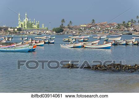 Stock Image - "Colorful fishing boats in the harbour, Mohijedin Sher Darga Sherif mosque at the back, Vizhinjam, Kerala, India, Asia". Fotosearch