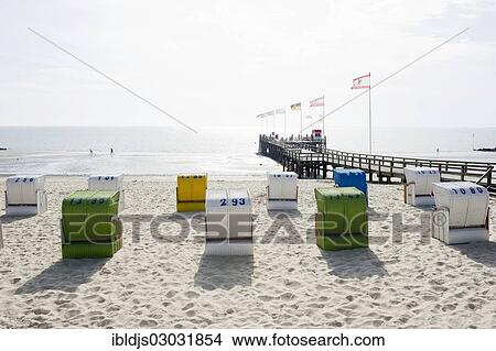 Picture - "Colourful roofed wicker beach chairs and a pier, Amrum, North Frisian Islands, Schleswig-Holstein, Germany, Europe". Fotosearch