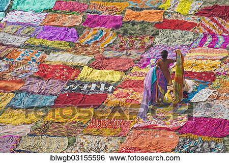 Stock Photograph - "Colourful saris are laid out on the sand for drying after washing, an Indian woman is collecting the dried saris, Agra, Uttar Pradesh, India, Asia". Fotosearch