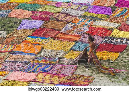 Stock Photo - "Colourful saris laying to dry after washing on a sandbank on the banks of the Yamuna River, an Indian woman is carrying the dried saris, Yamuna, Agra, Uttar Pradesh, India, Asia". Fotosearch