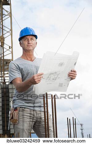 Stock Photo - "Construction worker wearing a hard hat and holding a building plan, Mannheim, Baden-Wurttemberg, Germany, Europe". Fotosearch