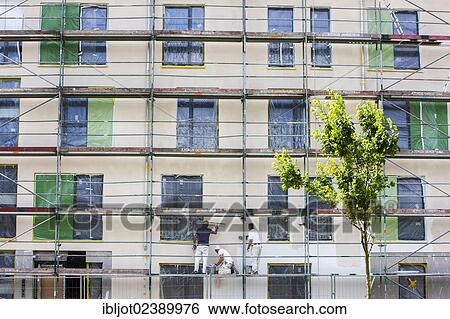 Stock Photograph - Construction workers plastering the facade of a new building after it was insulated. Fotosearch