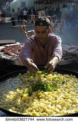 Picture - "Cook adds pieces of green peppers to a large pan containing potato stew at the annual All Saints Market in Cocentaina, Alicante province, Spain, Europe". Fotosearch