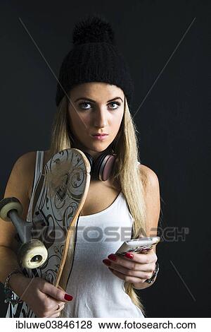 Stock Photo - "Cool young woman with a skateboard, headphones and a mobile phone". Fotosearch