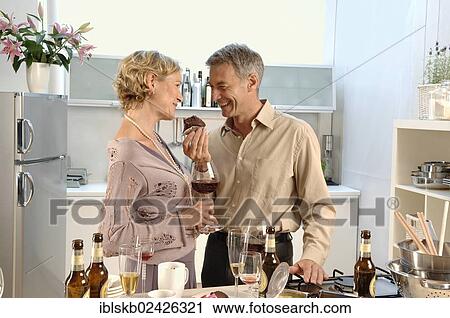 Stock Image - "Couple, 35-45, standing together in a messy kitchen after a party". Fotosearch