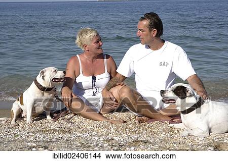 Picture - "Couple, 41, 50 years, with their dogs, Staffordshire Bull Terriers, on the beach". Fotosearch
