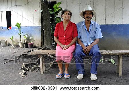 Stock Image - "Couple, 58 and 59, sitting on a bench in front of a house, La Sabaneta, Departamento Masaya, Nicaragua, North America". Fotosearch