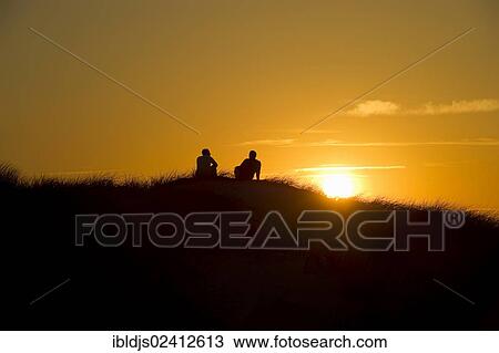Stock Image - Couple at sunset and dunes, Kniepsand in Nebel, Amrum, North Frisia, Schleswig-Holstein, Germany, Europe. Fotosearch
