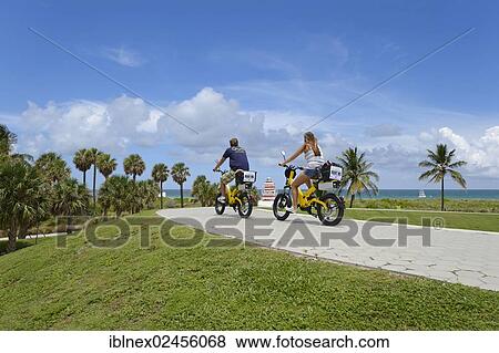 Stock Photo - "Couple riding electric bicycles, South Pointe Park, South Beach, Miami, Florida, USA". Fotosearch