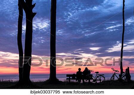 Stock Photography - "Couple sitting on a bench, silhouettes, sunset over the sea, Nienhagen, Mecklenburg-Western Pomerania, Germany, Europe". Fotosearch