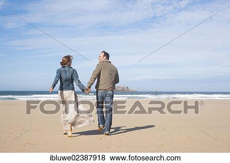 Stock Photo - Couple walking along the beach. Fotosearch