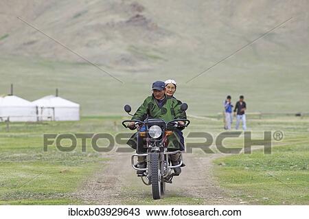 Stock Image - "Couple wearing the traditional deel, riding a motorcycle, Terkhiin Tsagaan Nuur, North Steppe, Arkhangai Aimag, Mongolia, Asia". Fotosearch