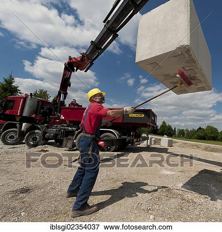 Stock Photo - "Crane operator cleaning the underside of a concrete block during a building site load test at a construction site in Fridolfing, Bavaria, Germany, Europe". Fotosearch