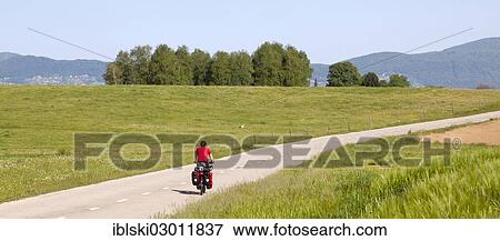 Stock Photo - "Cyclist on a lonely road in Kolpa Nature Reserve, near Crnomelji, Slovenia, Europe". Fotosearch