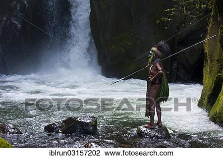 Stock Image - "Decorated and painted tribal chief standing in front of a waterfall in the Highlands, Paya, Highland, Papua New Guinea, Oceania". Fotosearch