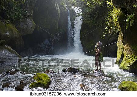 Stock Photograph - "Decorated and painted tribal chief standing in front of a waterfall in the Highlands, Paya, Highland, Papua New Guinea, Oceania". Fotosearch